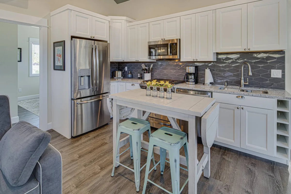 The view focuses on a cozy dining area adjacent to the kitchen. A solid wooden dining table sits next to stainless steel appliances and a contemporary hexagonal backsplash, fostering an inviting environment for shared meals and intimate gatherings.