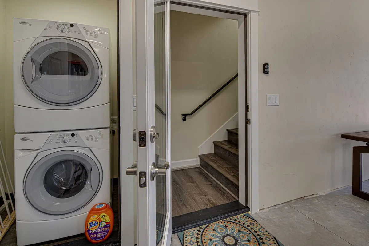 This image captures the front door and entryway area, with a washing machine visible to one side and a staircase leading upwards. The space is functional and inviting, suggesting a seamless transition from indoors to outdoors.