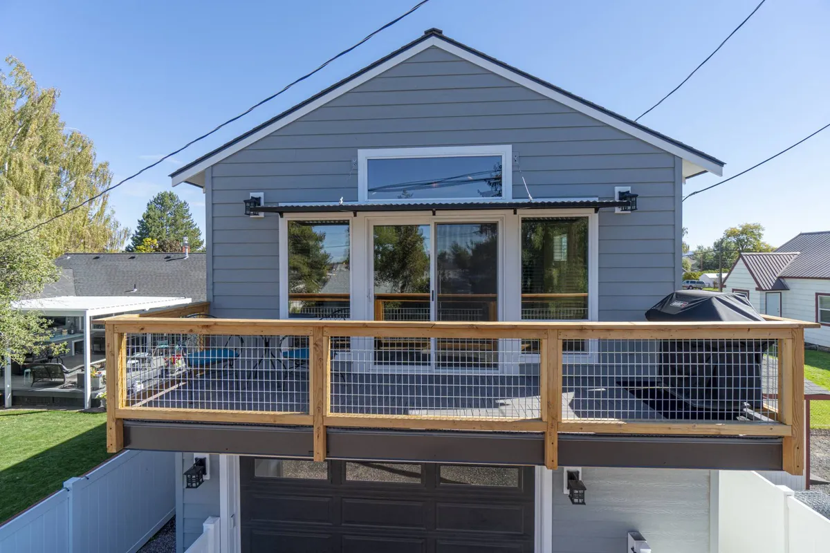This image features the front porch and large deck area with prominent deck railing, large windows, and inviting outdoor spaces. The scene evokes a welcoming atmosphere, perfect for gathering, relaxing, and enjoying sunset views. The deck appears spacious and set up for outdoor living.