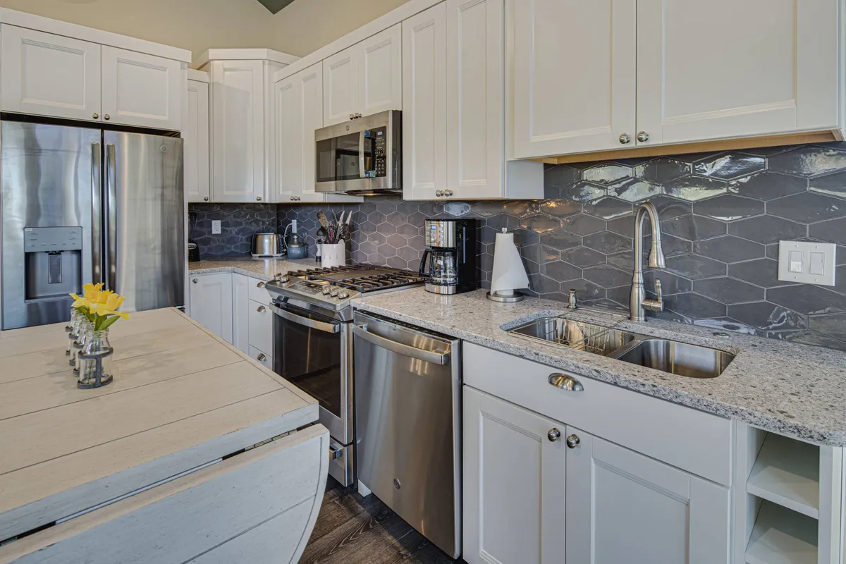 This image captures a modern kitchen with gleaming stainless steel appliances, polished granite countertops, a hexagonal tile backsplash, and a kitchen island adorned with fresh flowers. The overall atmosphere is bright and welcoming, ideal for meal preparation and gatherings.