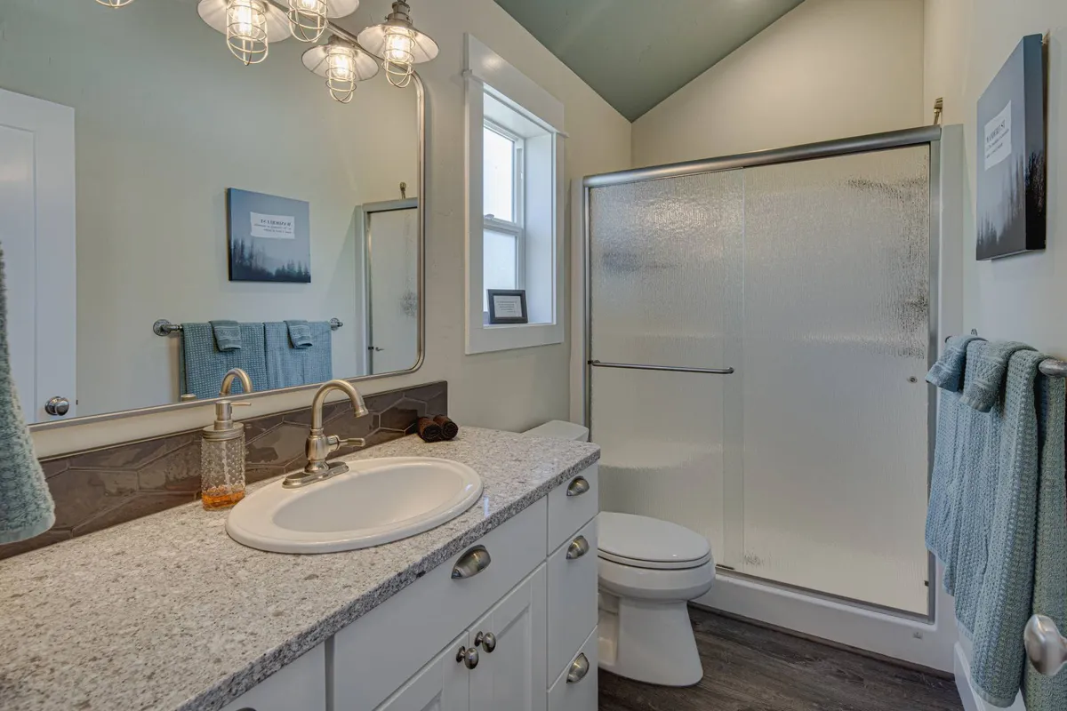 A pristine bathroom featuring a vanity with sink, a glass-enclosed shower, modern light fixtures, and a serene, refreshing atmosphere ideal for self-care and rejuvenation.
