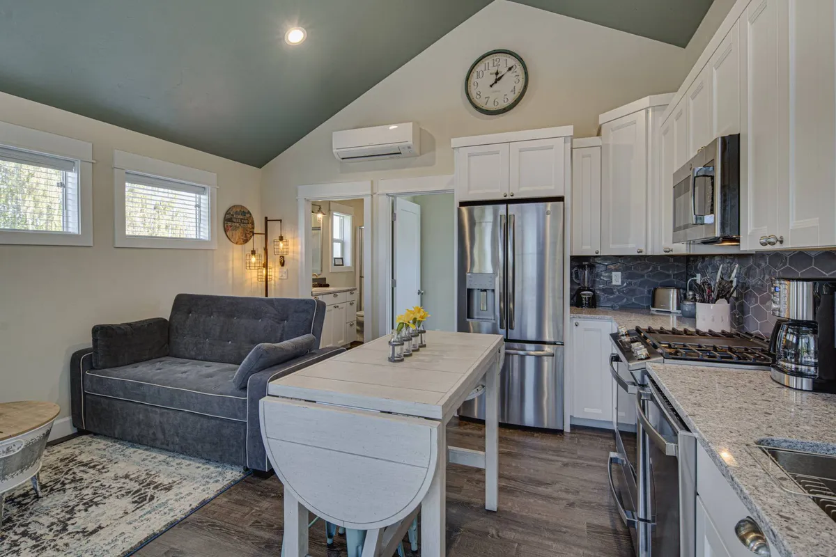 A cozy, modern interior living space with a comfortable sofa, dining table, and a well-equipped kitchen visible in the background. Sunlight softly illuminates the room, suggesting a peaceful spot to unwind after a busy day outdoors.