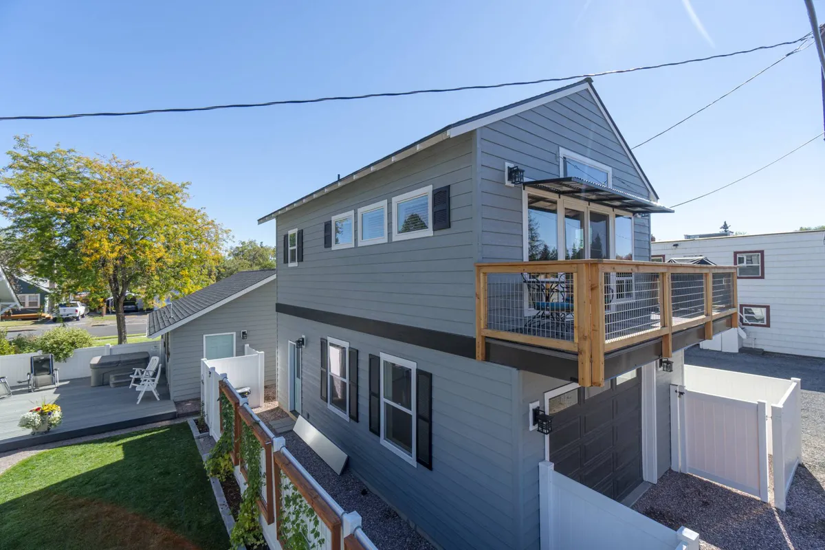 This image features the exterior of a modern property with a balcony, lush greenery, and a sunlit facade. The balcony and large windows suggest a close connection to the outdoors and provide natural light inside, reinforcing a tranquil, inviting atmosphere for relaxation or remote work.