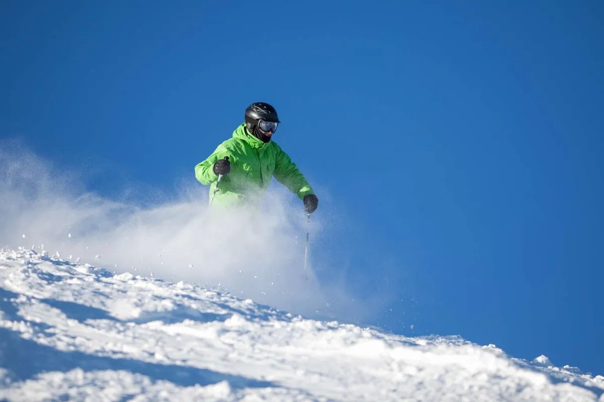 A dynamic exterior shot featuring a skier carving down a snowy slope with an impressive mountain backdrop. The scene is filled with energy, capturing the thrill and adventure of winter sports in a striking natural setting.